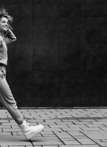 Young fashionable woman waking on the street and listening to music